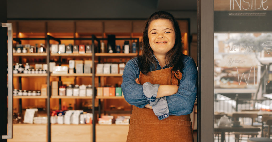 Cheerful woman with Down syndrome standing at the door of a shop